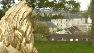 A gold statue of a lion with 20th Century housing behind.